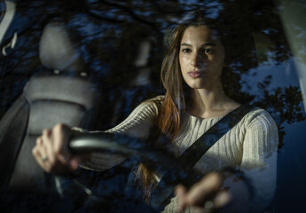 Obraz premium Young woman driving calmly at dusk in her car