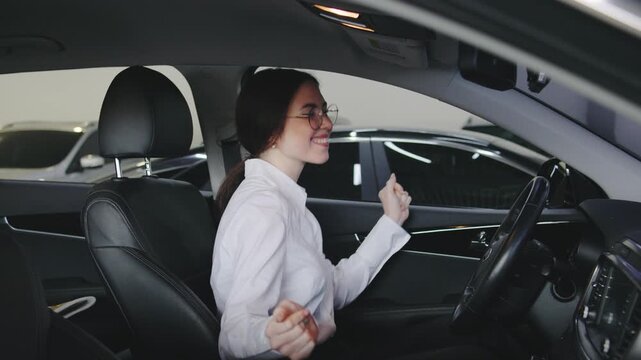 A female car saleswoman celebrates closing a deal by dancing in the front seat of a vehicle, thrilled after successfully selling a car at the dealership