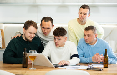 Men drink beer and try to help friend solve problems using laptop and the Internet