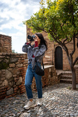 A young woman photographing with a camera in an ancient stone path, surrounded by historical architecture and greenery