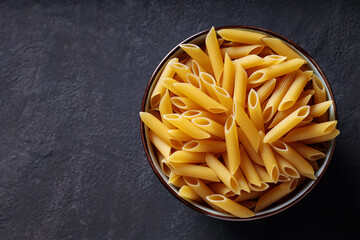 Dry Yellow Penne Pasta in Ceramic Bowl on Dark Background