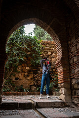 A woman taking photos with a camera in a stone-walled garden with ivy and cobblestone paths