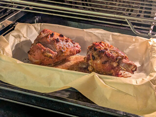 Raw poultry pieces seasoned and arranged in baking tray inside oven for cooking in Warsaw Poland home kitchen meal preparation. High quality photograph.