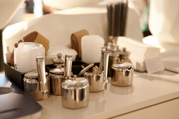 cafe condiment station with assorted sugar containers, napkins, stirrers, and cup sleeves. essential coffee shop setup offering customers convenience and organization in self-service environment.