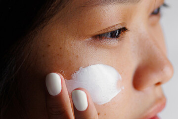 Asian young woman applying skincare cream to face for moisturizing routine