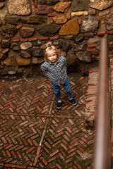 Child standing near stone wall, looking up with curiosity while exploring the ancient stone stairs and surroundings