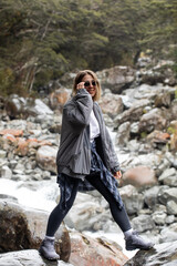 A woman hiking across rocky stones beside a mountain river in Arthurs Pass, New Zealand.
