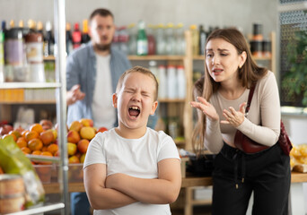 Capricious little boy crying in supermarket while his mom is trying to calm him down