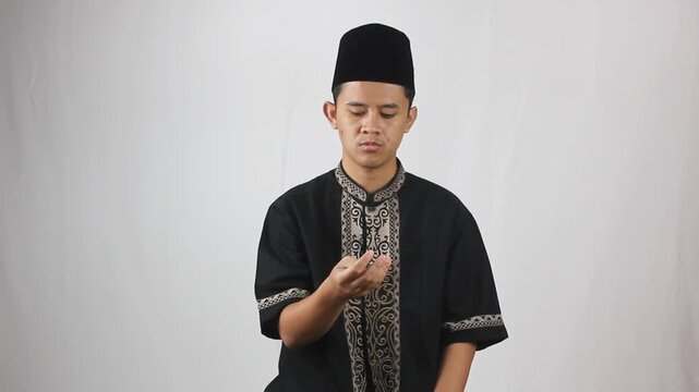 young asian man wearing muslim clothes reciting dhikr using his finger lines