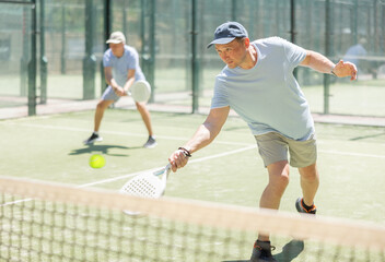 Elderly man and adult man playing doubles padel tennis on court