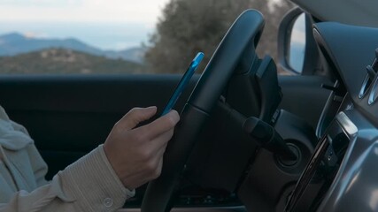 Woman using smartphone while driving modern car. Professional businesswoman dangerously texting on mobile phone while driving through scenic landscape, risking potential traffic accident