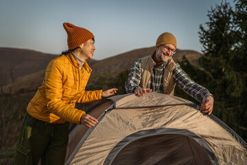 Happy couple camping outdoors setting up tent together