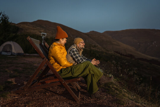 Couple relaxing on lounge chairs during mountain camping trip - Powered by Adobe