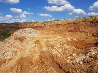 An open-pit quarry under a vibrant blue sky, featuring a large pile of crushed rock and...
