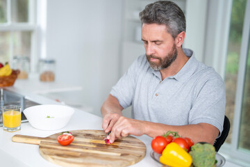 Mature Man eat breakfast in the kitchen on a morning. Guy eat vegetables for a healthy meal in his kitchen in the morning. Cozy kitchen. Morning breakfast in the white kitchen.