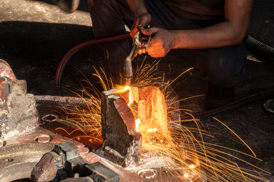 Hands of industrial worker using oxy-fuel torch to cut metal. Worker cutting metal with oxygen torch and flying sparks. Close-up of worker cutting metal with oxygen welding torch.