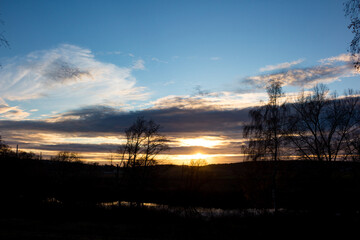 Fototapeta premium Stunning sunset over a tranquil landscape. Silhouetted trees frame the vibrant sky, reflecting in the calm water. A peaceful, golden hour scene