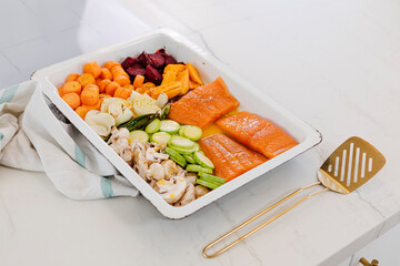 Preparing salmon fillets and various chopped vegetables for a healthy sheet pan dinner, ready for baking