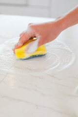 Hand cleaning kitchen counter with sponge and soap, washing marble surface in a bright home kitchen