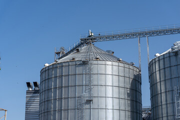 Harvesting facility features large grain silos with a clear blue sky in the background during midday, showcasing agricultural storage