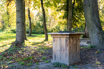 Wooden waste bin placed in a sunny park surrounded by trees during autumn afternoon