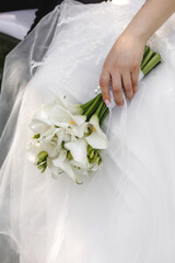close-up, the bride holds a bouquet of flowers in her hand against the background of a wedding dress