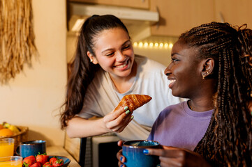 Two women sharing a cozy breakfast, smiling warmly while enjoying a flaky croissant and savoring the joy of togetherness