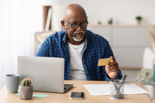 A senior African American businessman is engaged in online shopping at his workplace. He is using a laptop and holding a credit card while seated at a desk. - Powered by Adobe
