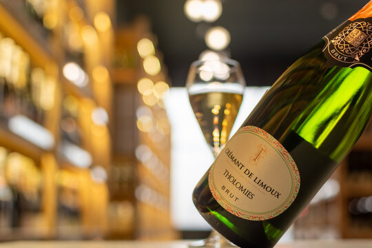 Dark green bottle of Cr&eacute;mant de Limoux Tholomies Brut with filled sparkling wine glass and blurred shelves completing the luxurious scene. Ukraine, Zhytomyr, October, 29, 2025