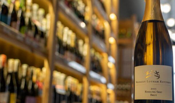 Bottle of Weingut Lothar Kettern Riesling Sekt Brut 2023 in softly lit wine shop with blurred shelves full of bottles in golden background . Ukraine, Zhytomyr, October, 29, 2025