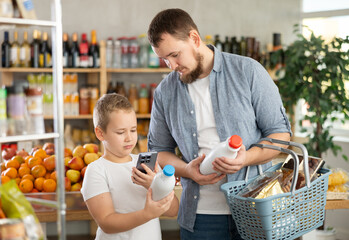 European man with son customer at shop scan QR code on milk bottle using phone camera. Client study composition, manufacturer information of product using application. Visitor examines product
