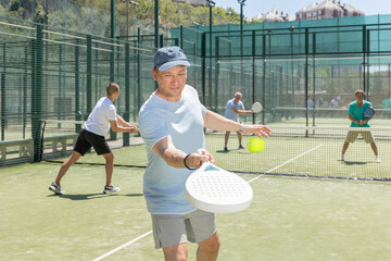 Padel game - man with partners plays on tennis court