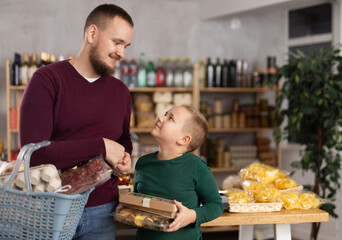 Positive guy and his son are choosing some products in grocery store