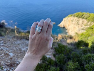 Landscape photo of an oval diamond engagement ring on hand with Croatian cliffs and horizon in background, Mediterranean engagement concept.