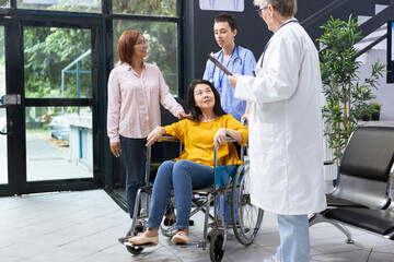 Medical staff assisting disabled asian woman to navigate hospital lobby during routine checkup. Focusing the conversation on accessibility needs and adjustments for independency.