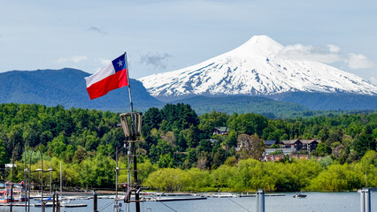 Close-up of the Chilean flag waving in the port of the city of Pucón, with the imposing Villarrica volcano in the background.