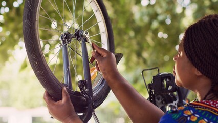 Sporty african american female cyclist uses spanner for tightening bicycle tire safely for outside cycling. Black woman performing bike maintenance with wrench as specialized work tool.