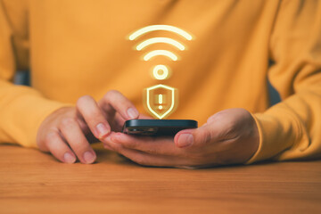 Close-up of hands using smartphone with glowing Wi-Fi and security shield warning icon, symbolizing cybersecurity, data protection, network privacy, online safety, and digital risk awareness.