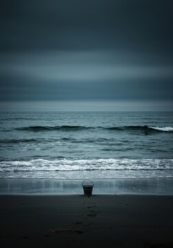 Symbolizing overwhelming scale, a tiny bucket stands near the shore attempting to capture the endless waves of the vast ocean ,large ,aspiration ,endless