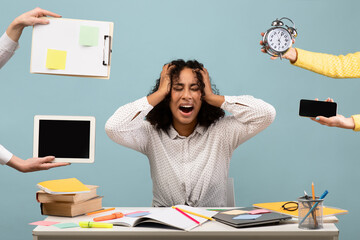 Young African American woman sits at a cluttered desk, surrounded by hands holding gadgets and a...