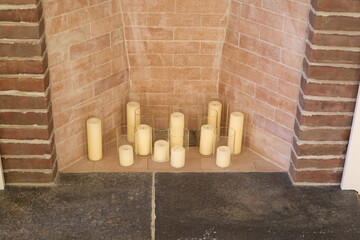 Cluster of pillar candles in fireplace, exposed brick hearth, cozy indoor decor
