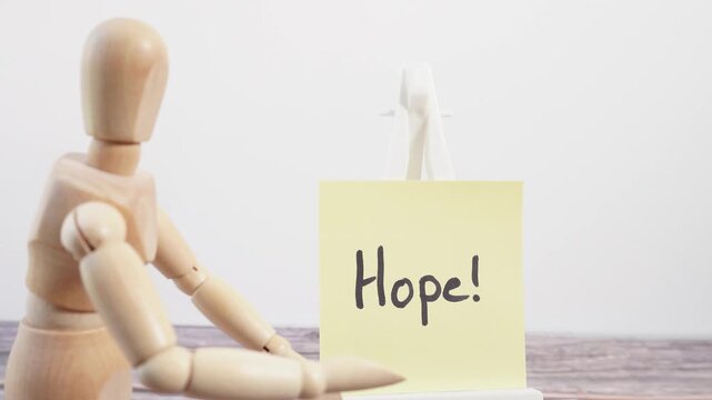 A wooden mannequin displays a sticky note with the word "Hope!"