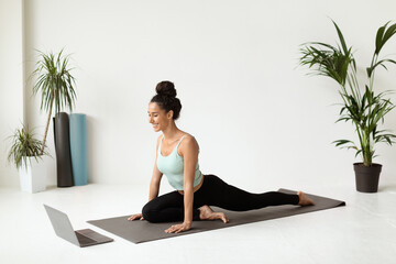 In a bright and open space, a young woman practices stretching on a fitness mat while engaging with...
