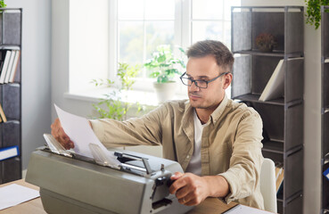 Writer with old typewriter typing book or new article in office. Busy man in glasses holding piece...