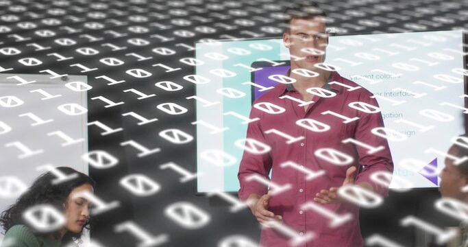 Leading White man in red shirt presenting in conference room, with display screen and binary data