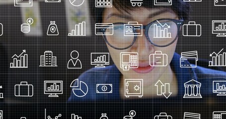 Chinese professional wearing blue top and glasses analyzing financial icons on monitor in office