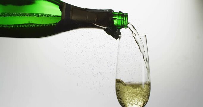 Green champagne bottle tilting and pouring champagne, filling flute, bubbles rising, flow slowing