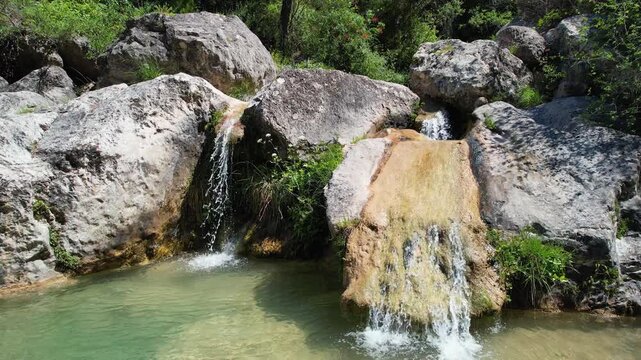 Forward reveal aerial shot of small waterfalls in Gorg Gorge (Barranc del Gorg) on sunny summer day. La Febr&oacute;, Tarragona, Spain.