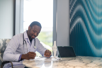 African doctor with stethoscope with medical report while working on laptop and medical documents...