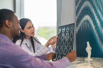 Woman doctor explaining brain CT scan results to male patient with medical consultation sitting at...
